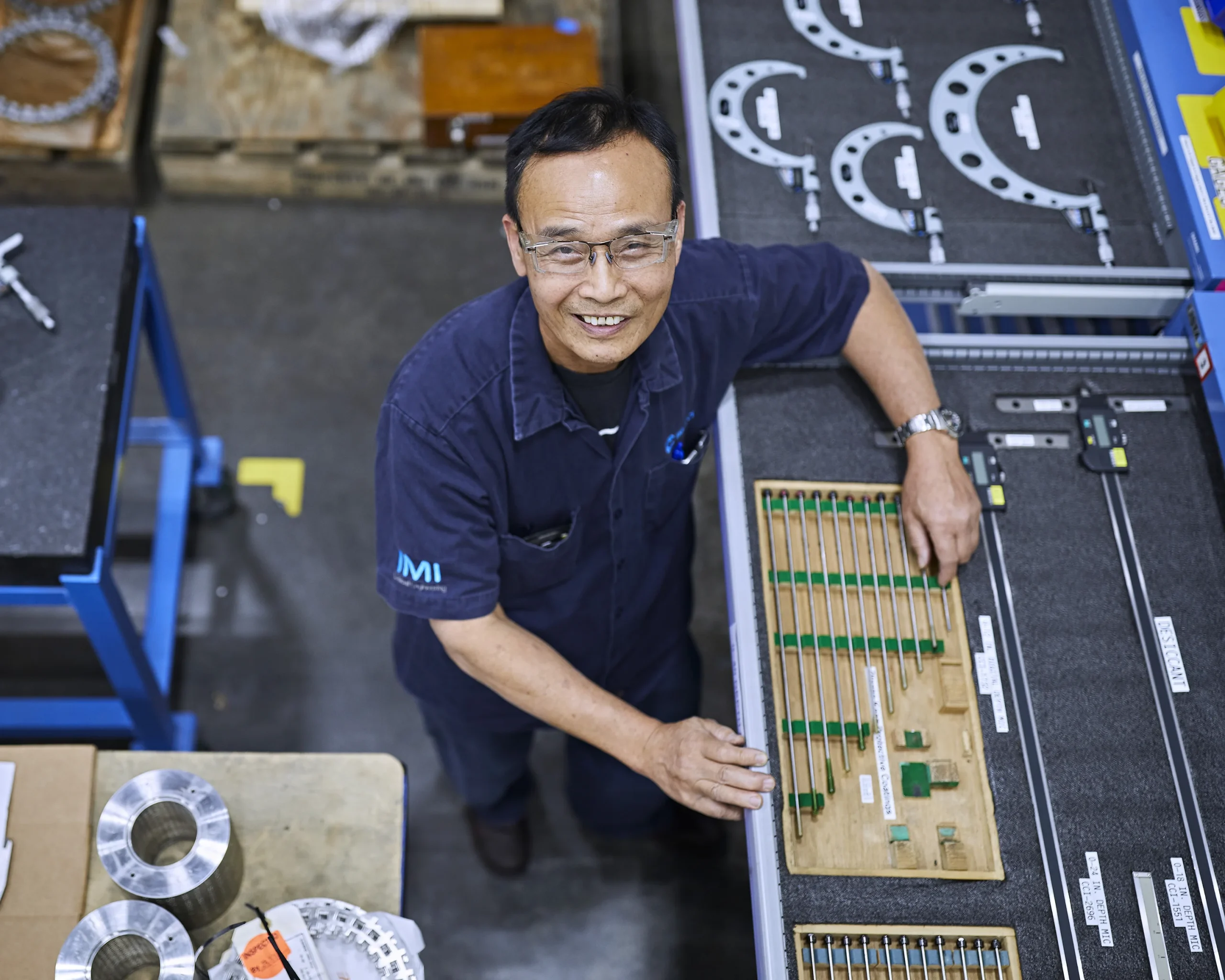 Man at IMI manufacturing site gazes up amid a network of inspection equipment, ensuring precision and quality control.