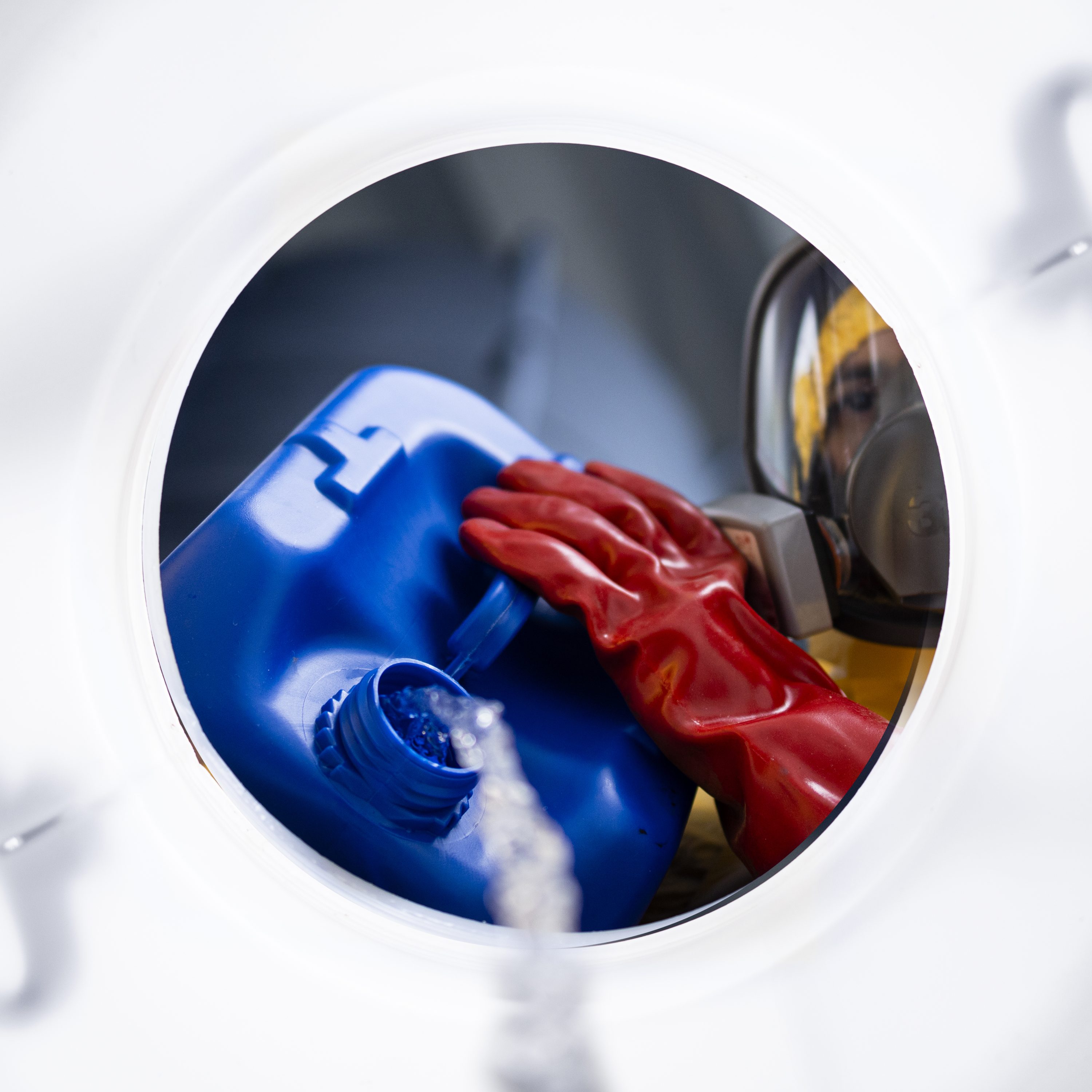 Chemical worker in protective suit, blending acids for industry inside a barrel.