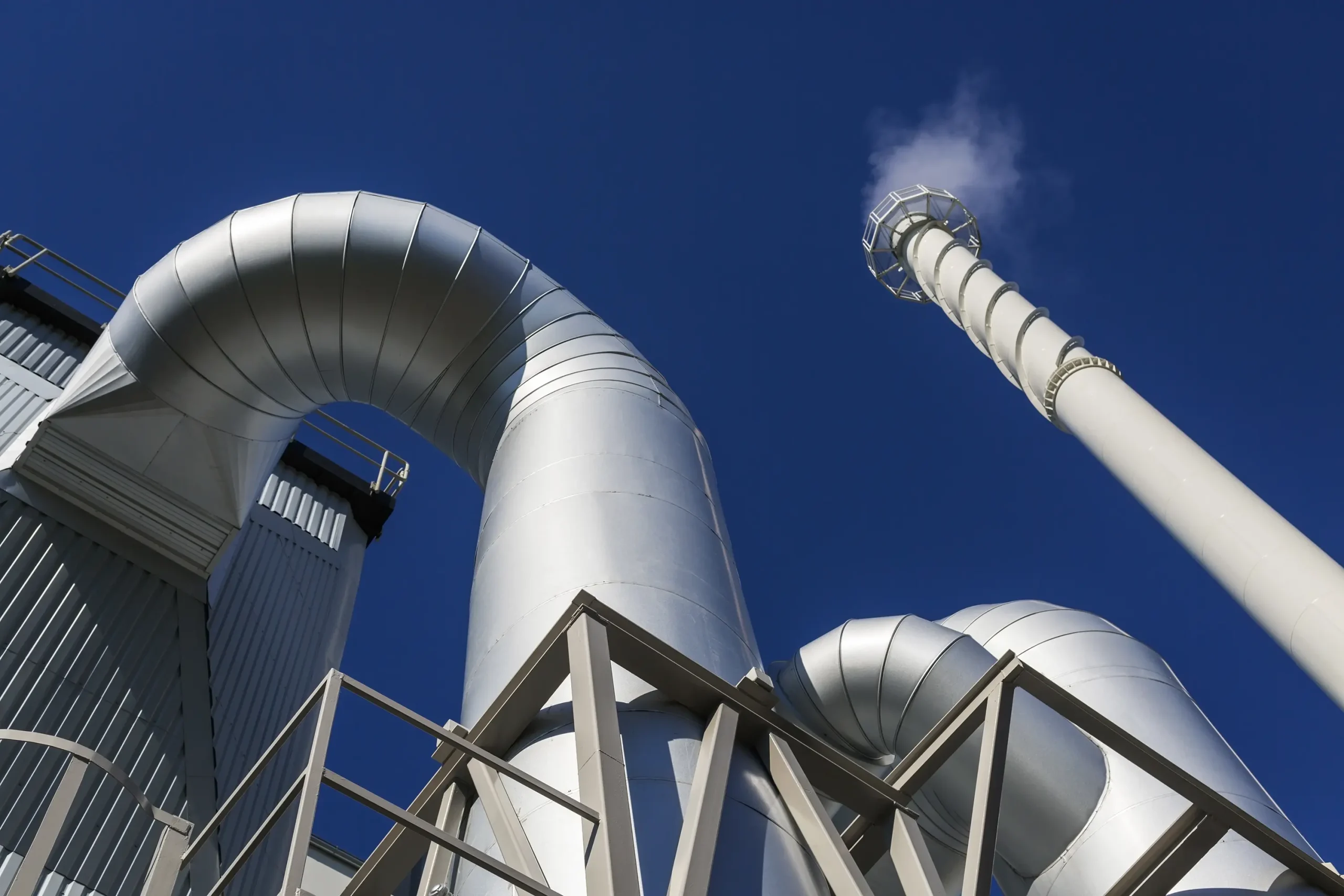 A metallic spiderweb of pipes emitting steam from a combined heat and power plant, showcasing the role of control valves in regulating the flow of steam