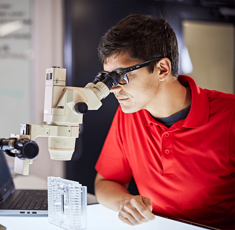 Norgren engineer inspects product with microscope, focused and precise. Expertise shines as they examine intricate details for quality control.